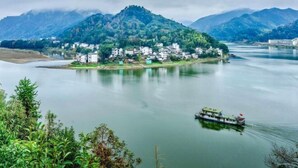 A river with a boat, a small island with buildings, and mountains in the background.