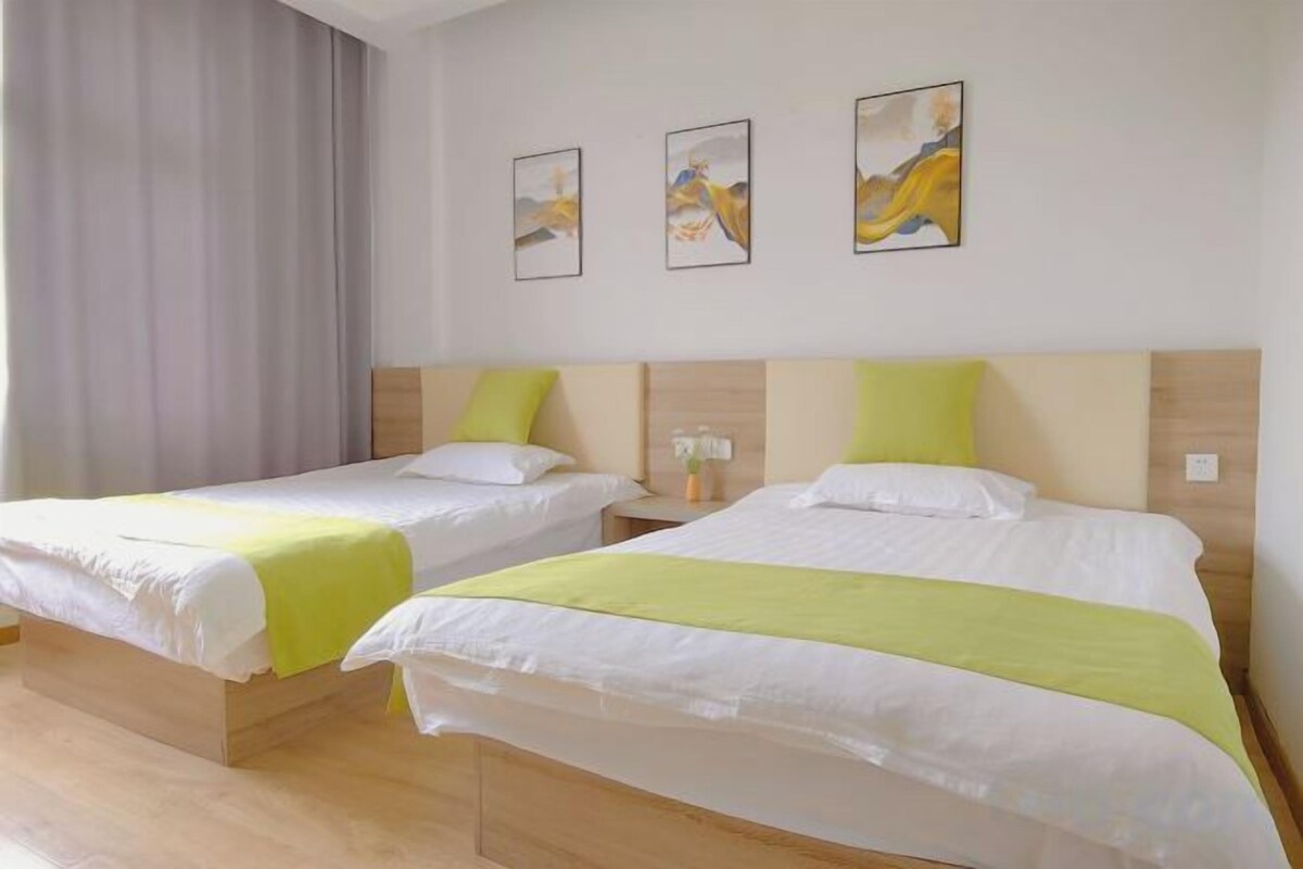 Two single beds with wooden headboards and white bedding, a gray curtain, and three framed artworks on the wall.