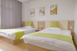 Dos camas individuales con cabeceras de madera y ropa de cama blanca, una cortina gris y tres cuadros en la pared.