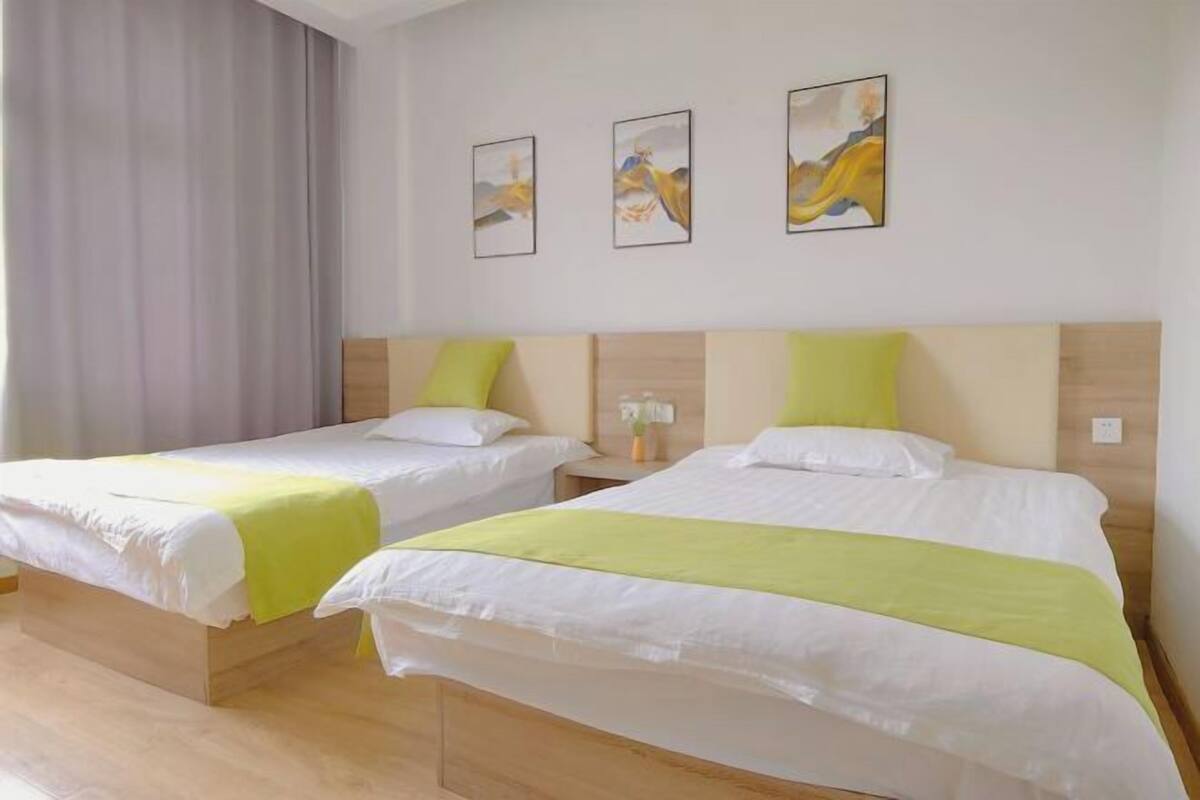 A hotel room with two beds, a wooden headboard, a nightstand with a lamp, and three paintings on the wall.