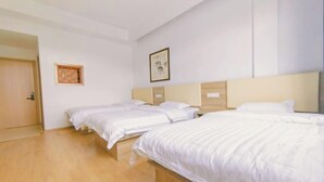 A hotel room with three beds, a wooden floor, a door, and a framed picture on the wall.