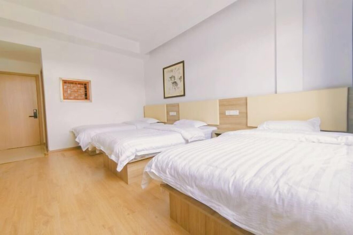 A hotel room with three beds, a wooden floor, a door, and a framed picture on the wall.