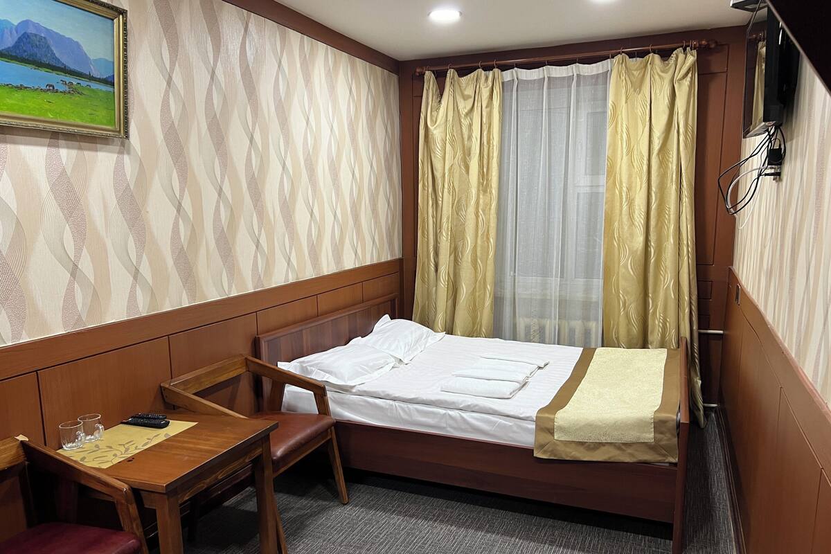 A hotel room with a single bed, a wooden desk, a chair, and a painting on the wall.