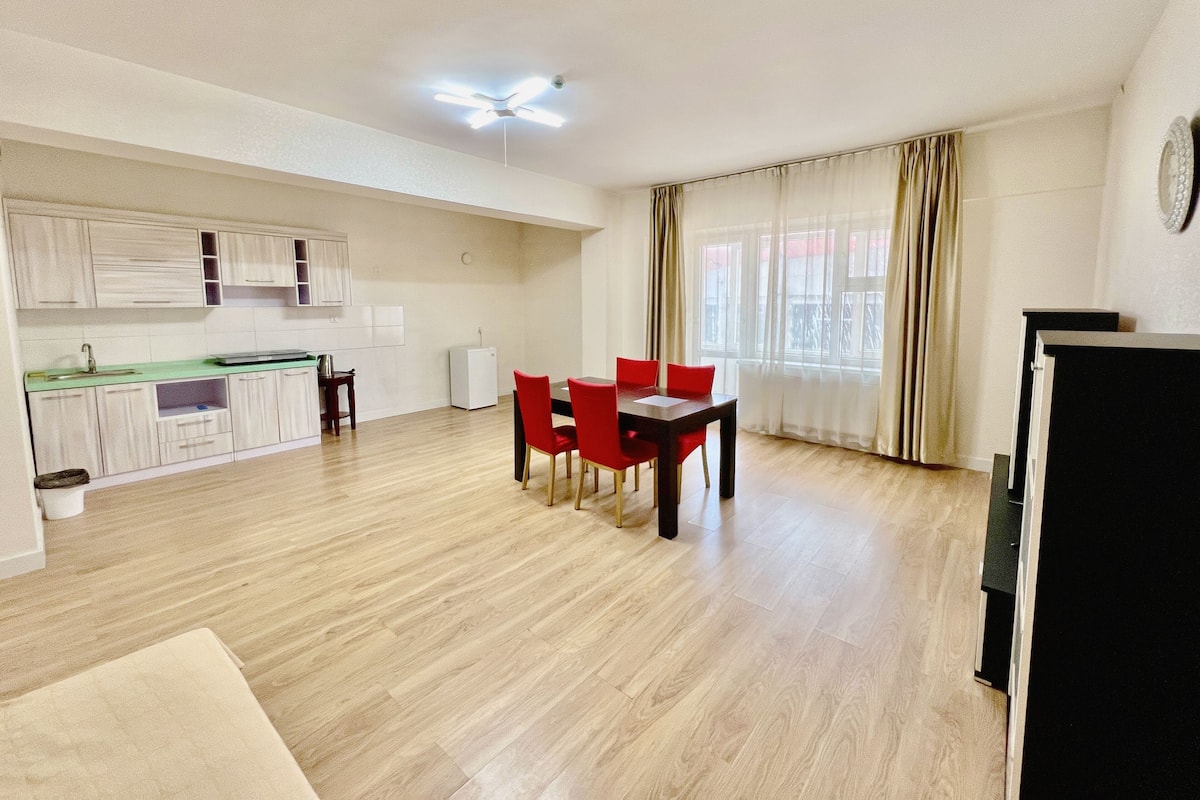 A modern apartment with a kitchen, dining area, and a large window with curtains.
