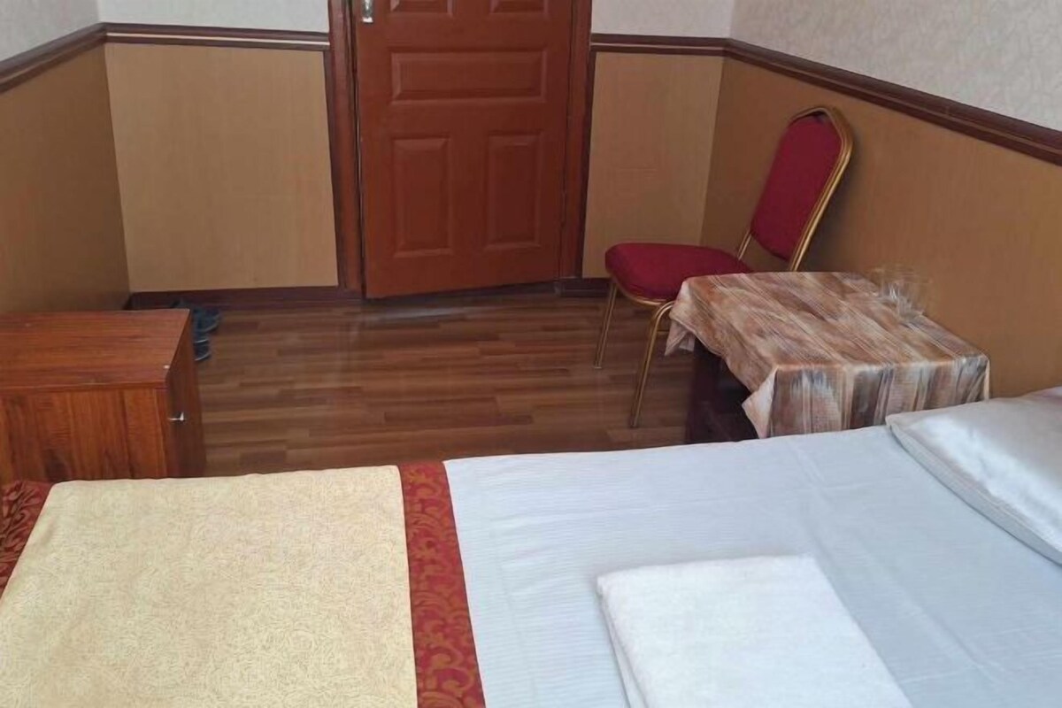A hotel room with a wooden floor, a bed with white linens, a small wooden table, a red chair, and a wooden wardrobe.