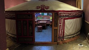A traditional tent-like room with a patterned entrance, a small stool, and a bed with a patterned bedspread. - Negdelchin Hotel & Service Apartment (Ulaanbaatar)