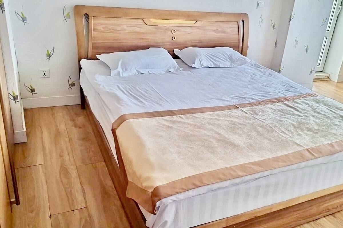 A large bed with a wooden headboard, white bedding, and a beige accent.