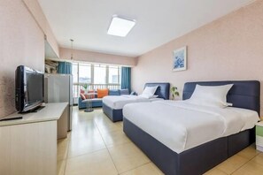 A hotel room with a bed, a desk with a television, a sofa, and a window with curtains.