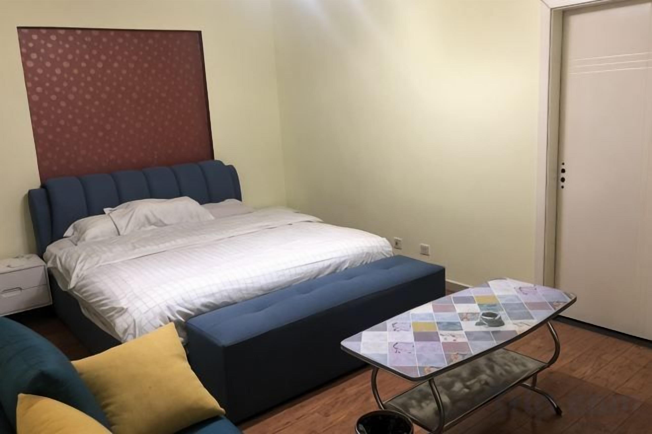 A bedroom with a bed, a sofa, a small table, and a door.
