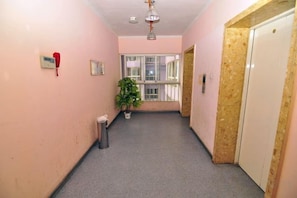 Un couloir avec une poubelle, une plante en pot, un téléphone rouge et une porte au fond.