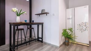 A modern kitchen with a white refrigerator, a wooden bar counter with stools, a potted plant, and pendant lighting. - Caiyun Jiayuan (Nanping Street Old Street Kunming) (Kunming)