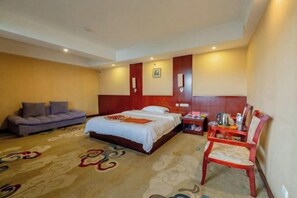 Una habitación de hotel con cama, sofá, sillón, mesita de noche y piso alfombrado.