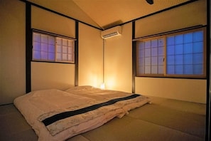 A traditional Japanese-style room with tatami flooring, a futon bed, sliding shoji doors, and a ceiling-mounted air conditioning unit. - Kyoran Suigetsutei (Kyoto)