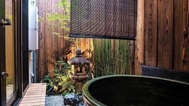 Un terrazzo in legno con una vasca idromassaggio, un lanternino e un recinto in bambù.