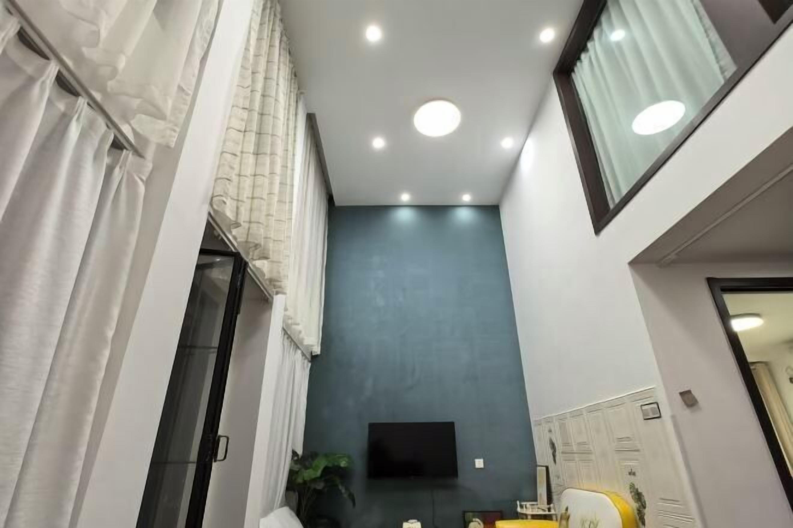 Un couloir étroit avec un téléviseur à écran plat fixé au mur, une plante en pot et une chaise jaune.