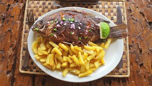 Un plato de pescado frito con papas fritas y una cuña de limón, sobre un mantel tejido.