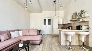 Een modern appartement met een roze bank, een eettafel en een keuken met witte kastjes, plus een bar met barkrukken.