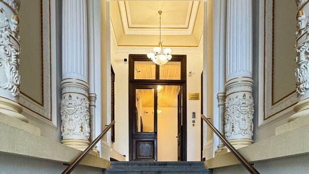 Een statige trap met versierde zuilen, die leidt naar een goed verlicht interieur.