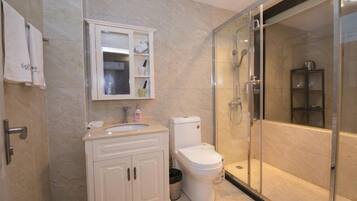 A bathroom with a glass shower enclosure, a toilet, a sink with a cabinet, and a mirror.