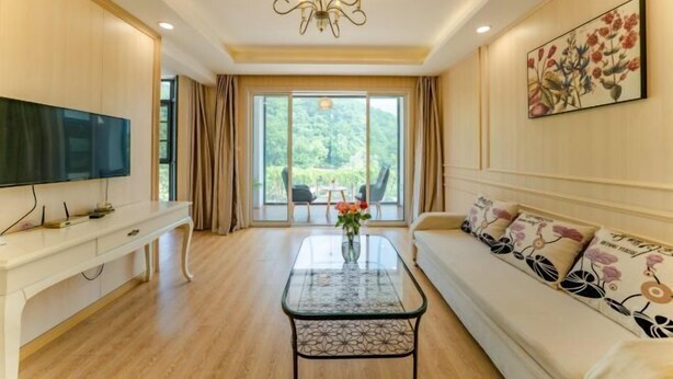 A spacious living room with a large flat-screen TV, a glass coffee table, a sofa with floral cushions, and a painting on the wall. - Yin Xiang Jiang Nan Inn (Yixing)