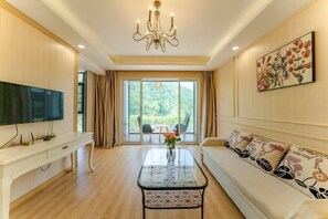 Un salón espacioso con un televisor de pantalla plana grande, una mesa de centro de cristal, un sofá con cojines estampados y un cuadro en la pared.
