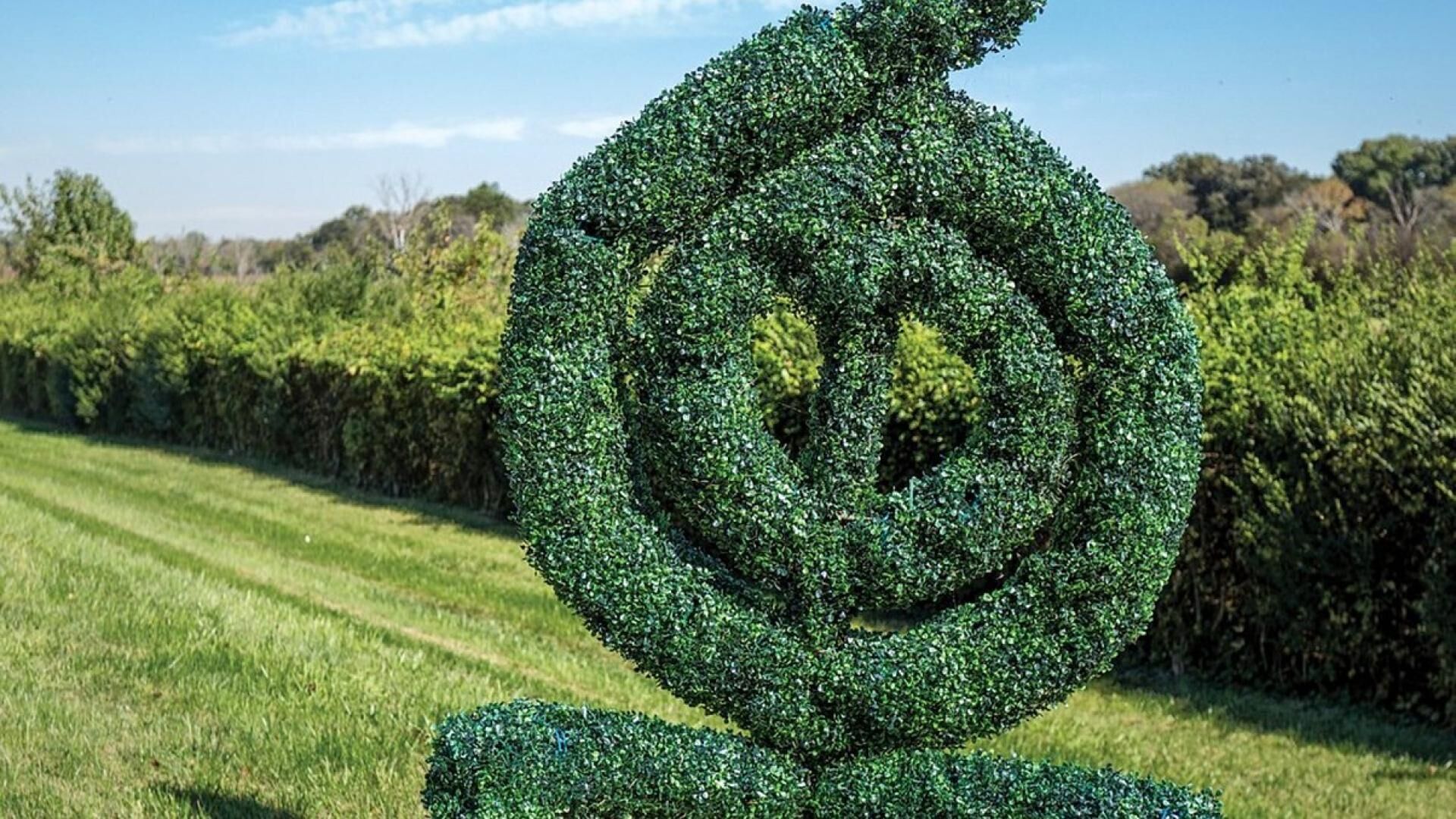 Escultura de sebe em espiral em um campo gramado.