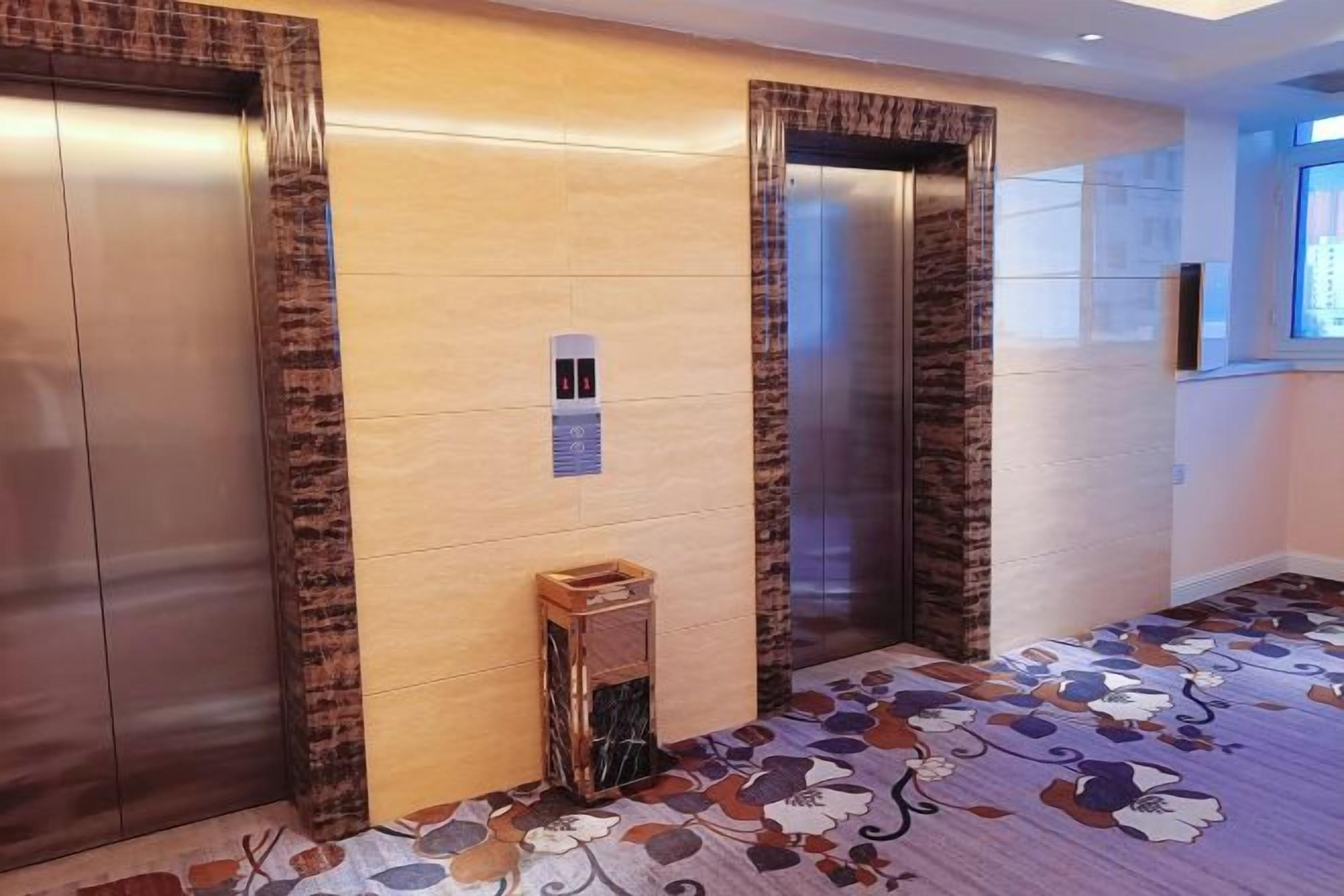 Zona de ascensores con dos elevadores, un panel de control en la pared y una alfombra estampada.