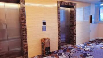 Zona de ascensores con dos elevadores, un panel de control en la pared y una alfombra estampada.