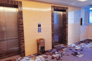 Zona de ascensores con dos elevadores, un panel de control en la pared y una alfombra estampada.