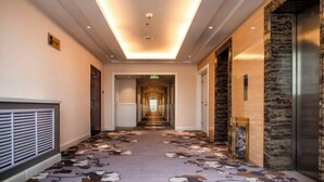 A hotel corridor with patterned carpet, a central light fixture, and a view into the hallway. - Huilong Dasha Hotel (Chengde)