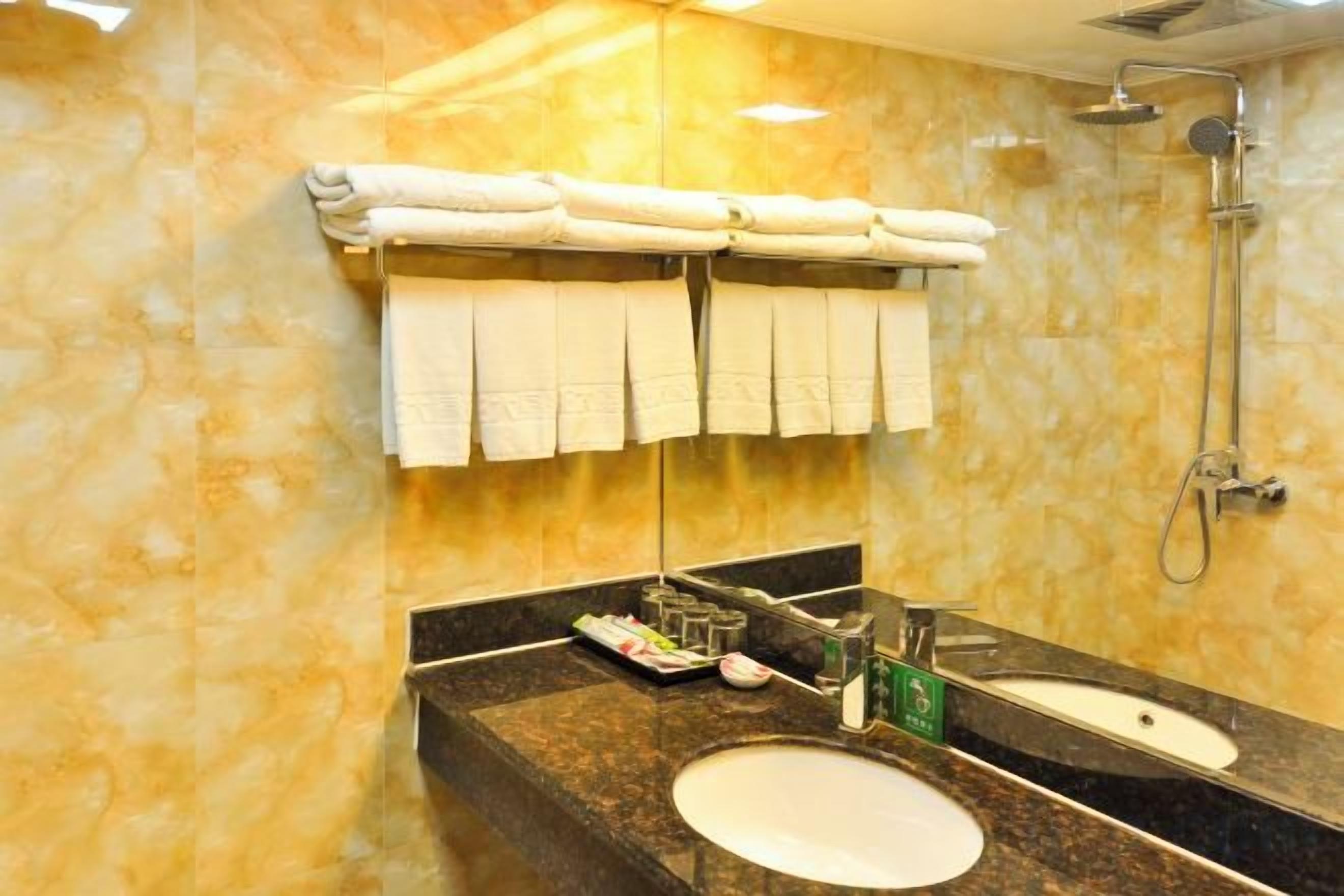 A bathroom with a marble wall, a double sink, a mirror, and a shower.