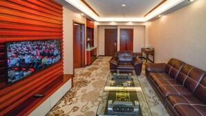 A modern living room with a flat-screen TV, leather sofas, a glass coffee table, and a patterned carpet. - Huilong Dasha Hotel (Chengde)