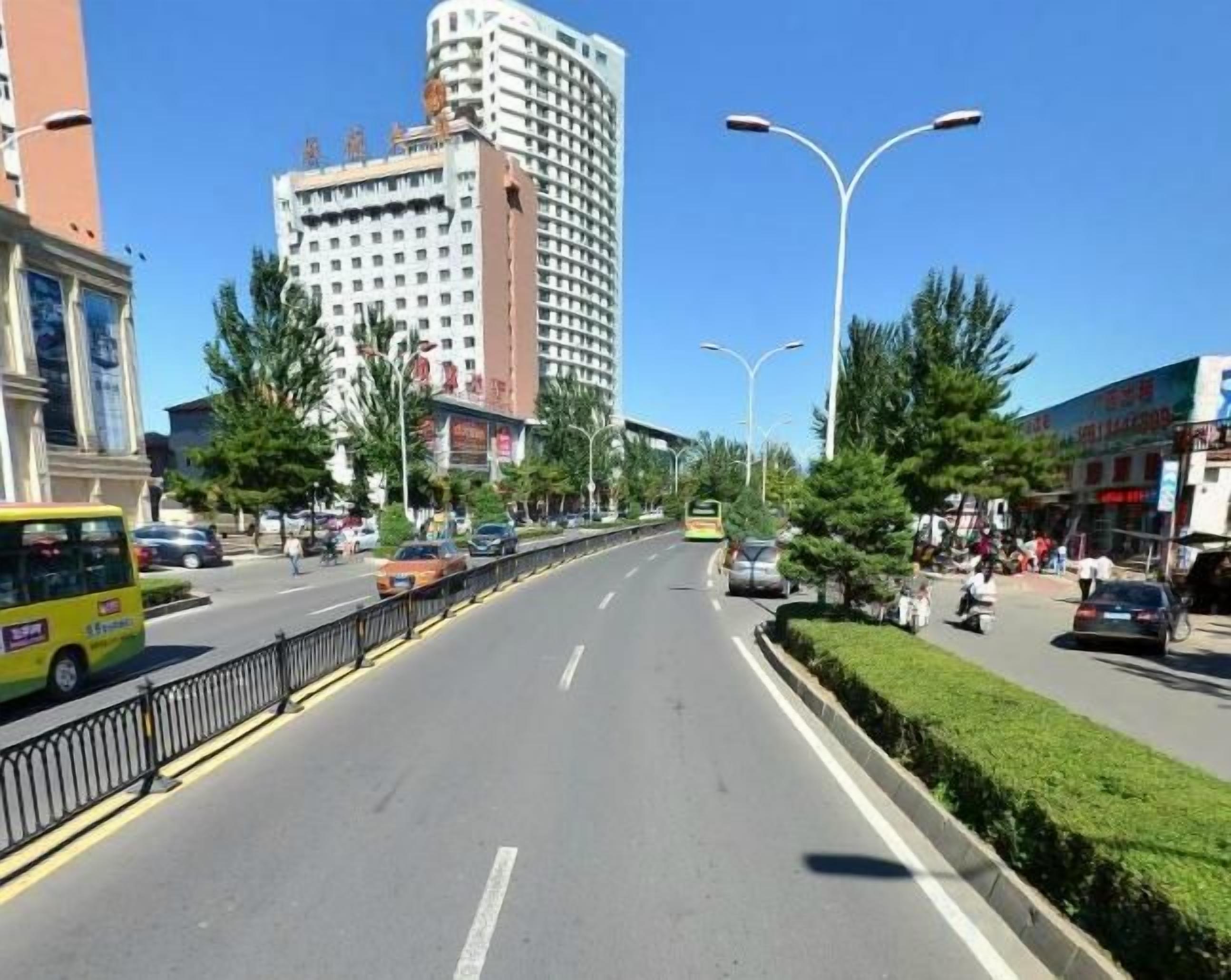 Una avenida urbana con varios carriles, vehículos, un autobús amarillo y peatones.
