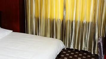 Una cama con sábana blanca y manta estampada, cortinas con degradado amarillo y blanco, y una vista parcial de una pared roja.