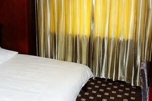 Una cama con sábana blanca y manta estampada, cortinas con degradado amarillo y blanco, y una vista parcial de una pared roja.