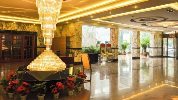 A lobby with a large chandelier, marble walls, and potted plants. - Huilong Dasha Hotel (Chengde)