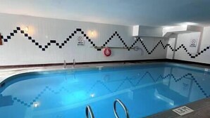 Une piscine intérieure avec des lignes de démarcation claires pour les couloirs, un panneau de sécurité et une bouée de sauvetage fixée au mur.