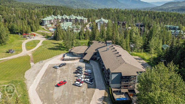 Un complexe hôtelier comprenant plusieurs bâtiments, un parking avec de nombreuses voitures et un paysage montagneux en arrière-plan.