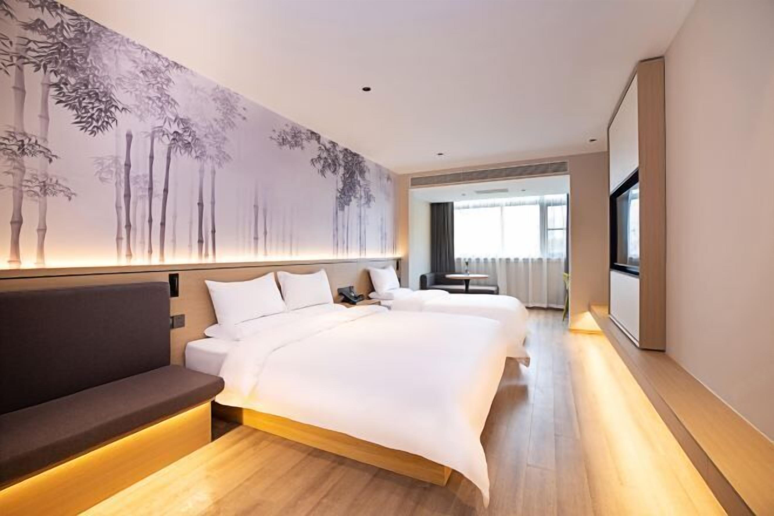A modern hotel room with a large bed, a sofa, and a wall mural.