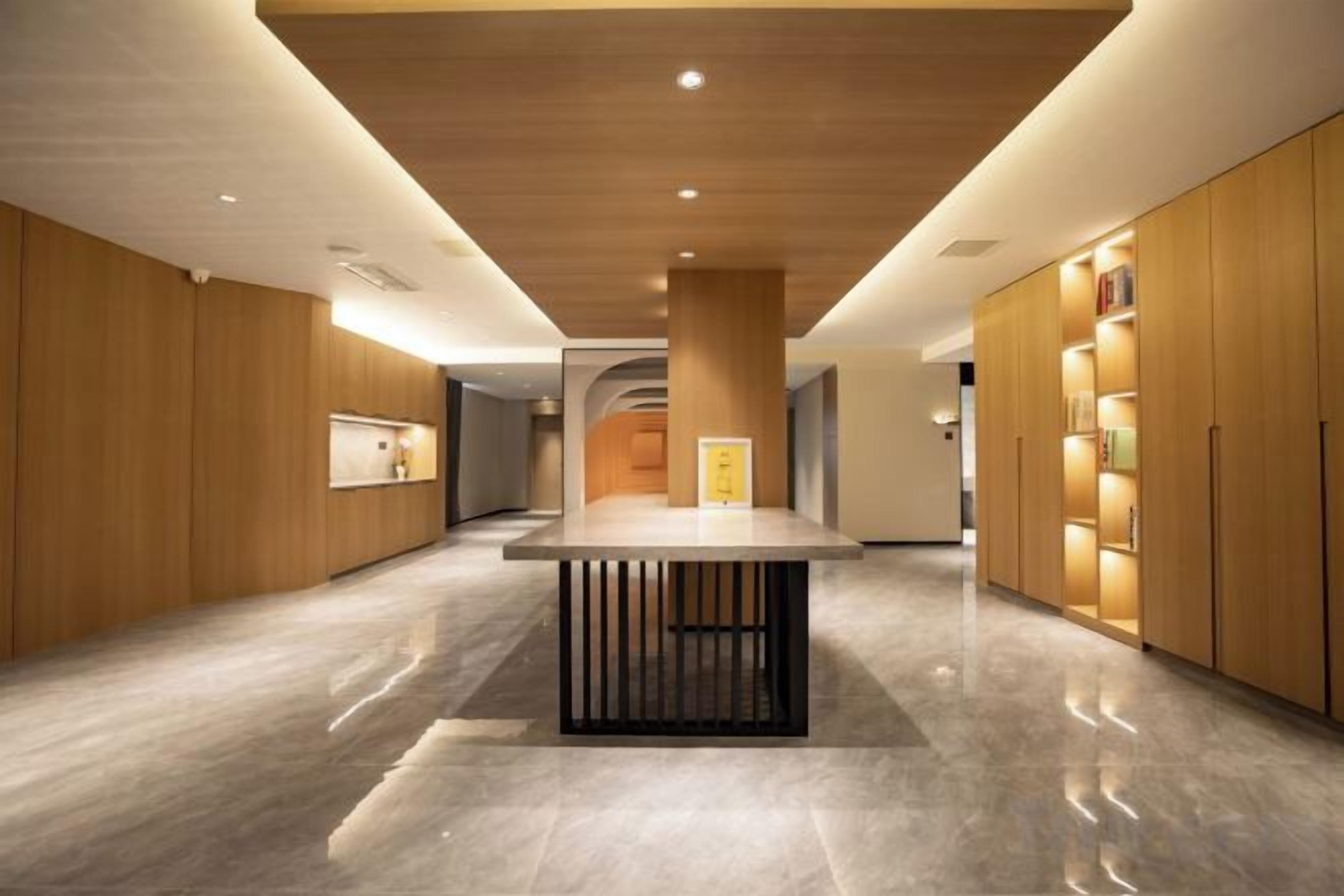 Un hall d’hôtel moderne avec un comptoir d’accueil central, des panneaux de bois et un sol en marbre.