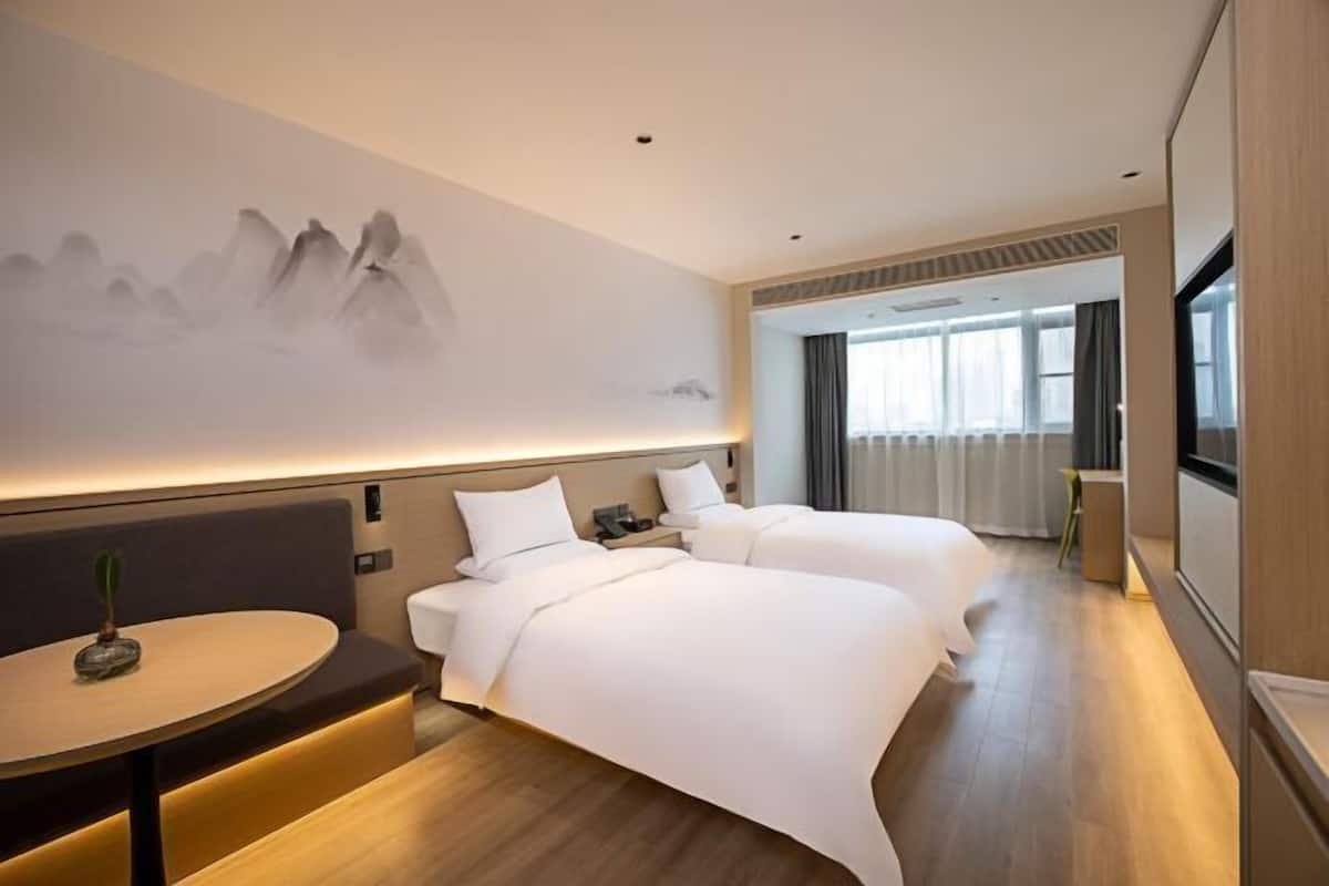 Habitación de hotel con dos camas, una mesa redonda, televisión montada en la pared y un ventanal grande.