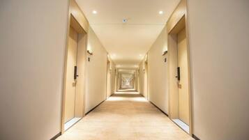 A long, narrow hotel corridor with doors on both sides and a carpeted floor.