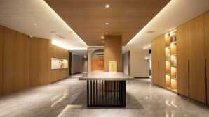 A modern hotel lobby with wooden panel walls, a central table with a black base, and built-in bookshelves on the right. - Songguo Hotel (Zhengzhou Tongbai Road Central Hospital Metro Station) (Zhengzhou)