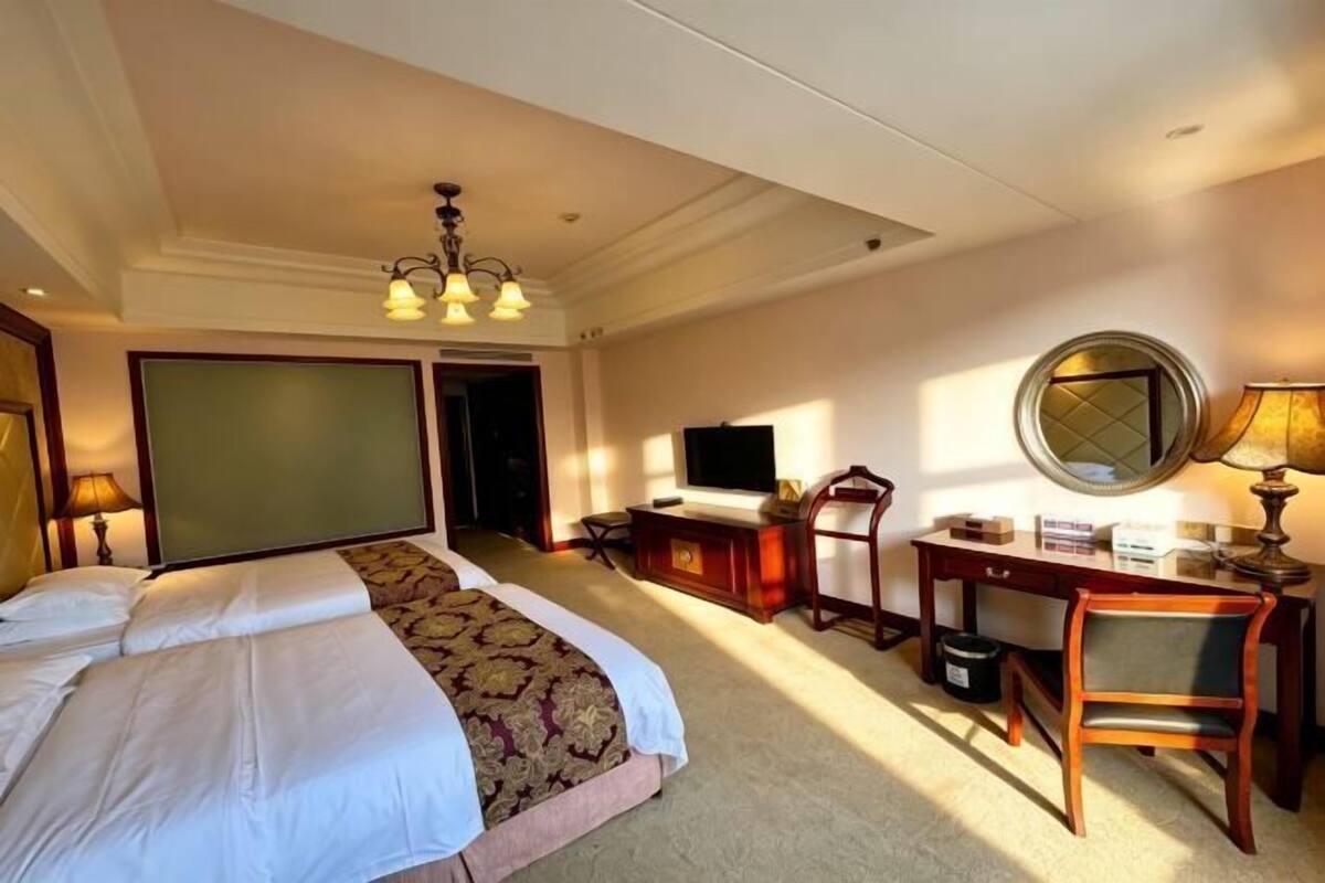 A hotel room with a bed, desk, chair, television, and a large mirror.