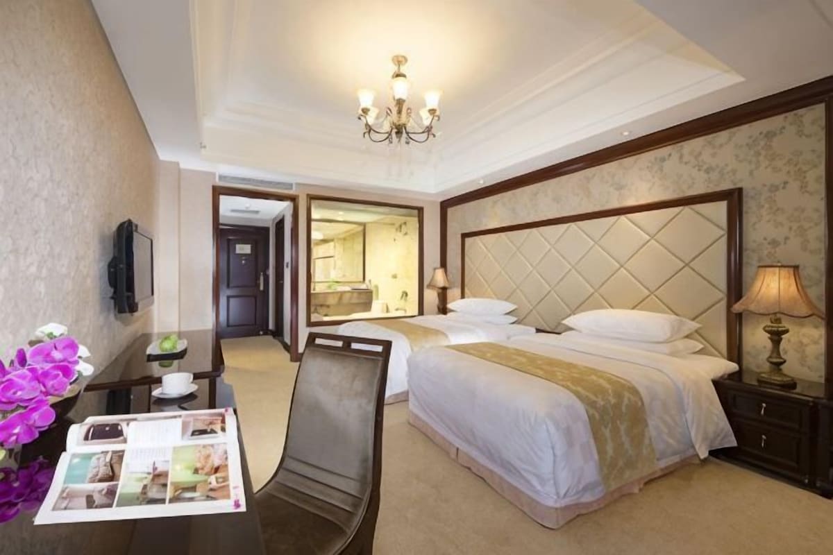Une chambre d’hôtel comprenant un lit, une table de chevet, une lampe, une chaise, un bureau avec un vase de fleurs et un magazine.