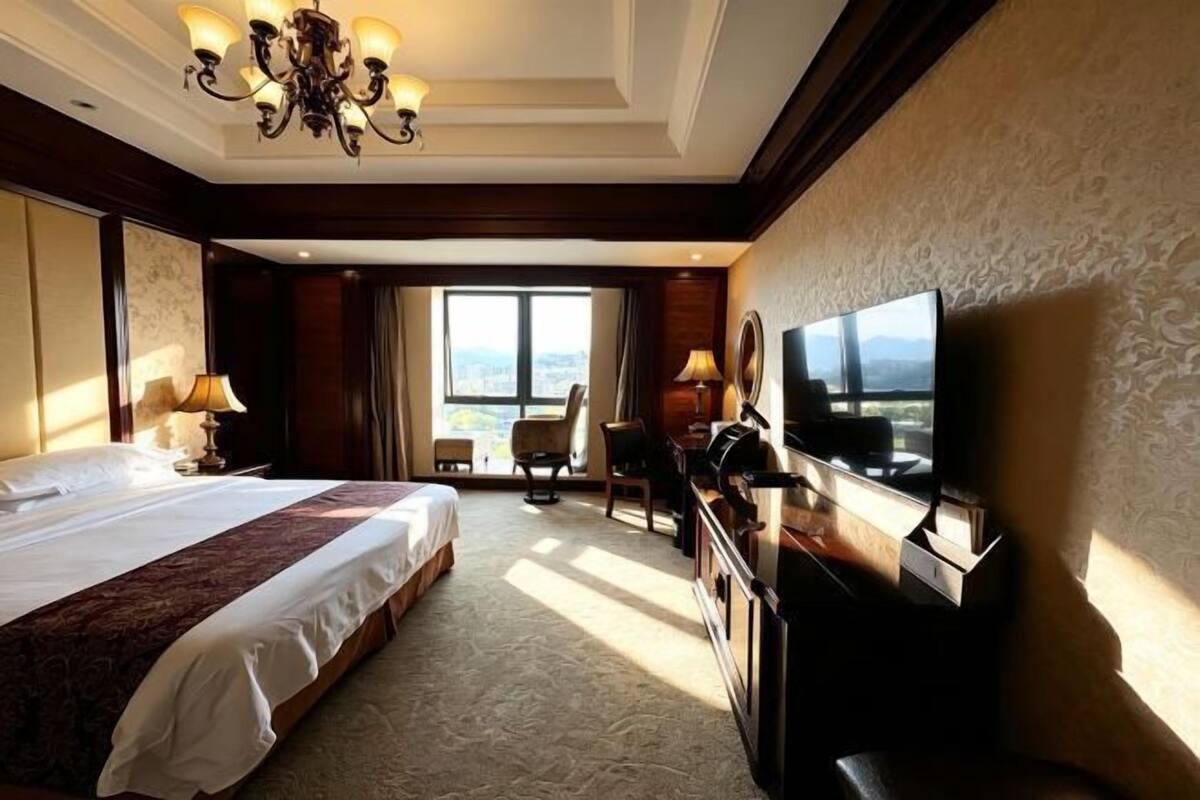 A hotel room with a large bed, a TV, a desk, and a view of the city.