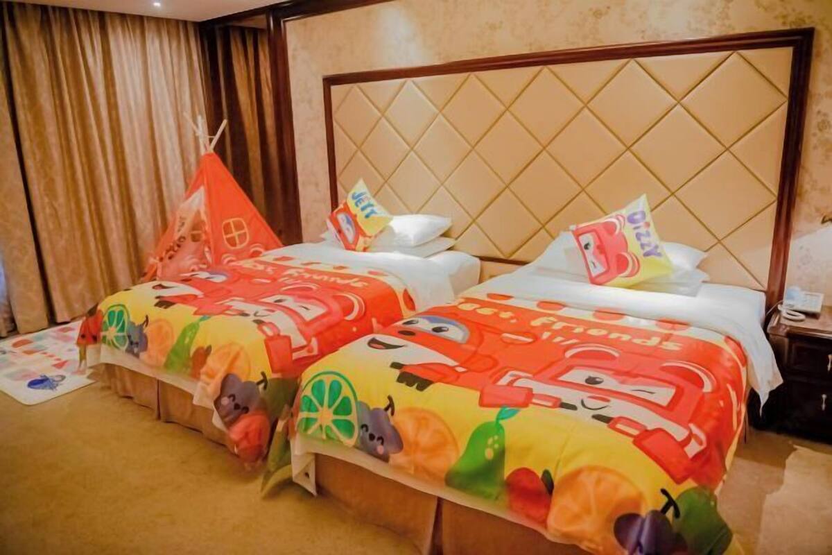 A hotel room with two beds, each with colorful bedding and a cartoon theme. There is a small table with a lamp and a nightstand with a phone.