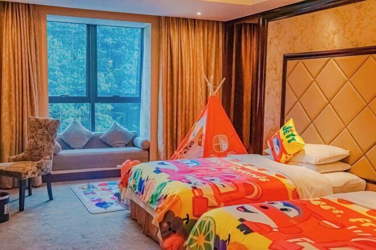 A hotel room with a large window, a sofa, a bed with colorful bedding, and a teepee structure.