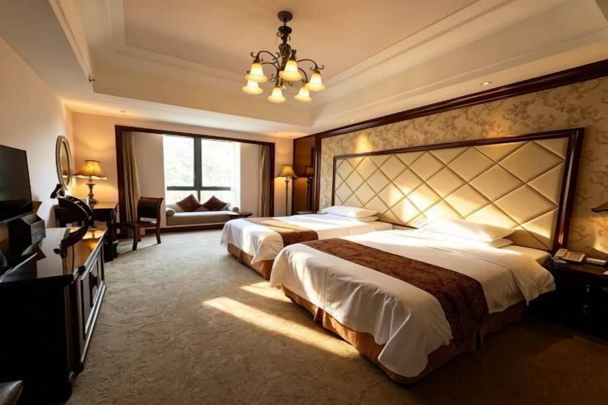 A hotel room with two beds, a chandelier, a television, and a desk.