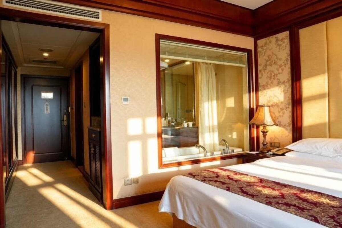 A hotel room with a large bed, a mirror, a nightstand, and a window with curtains.
